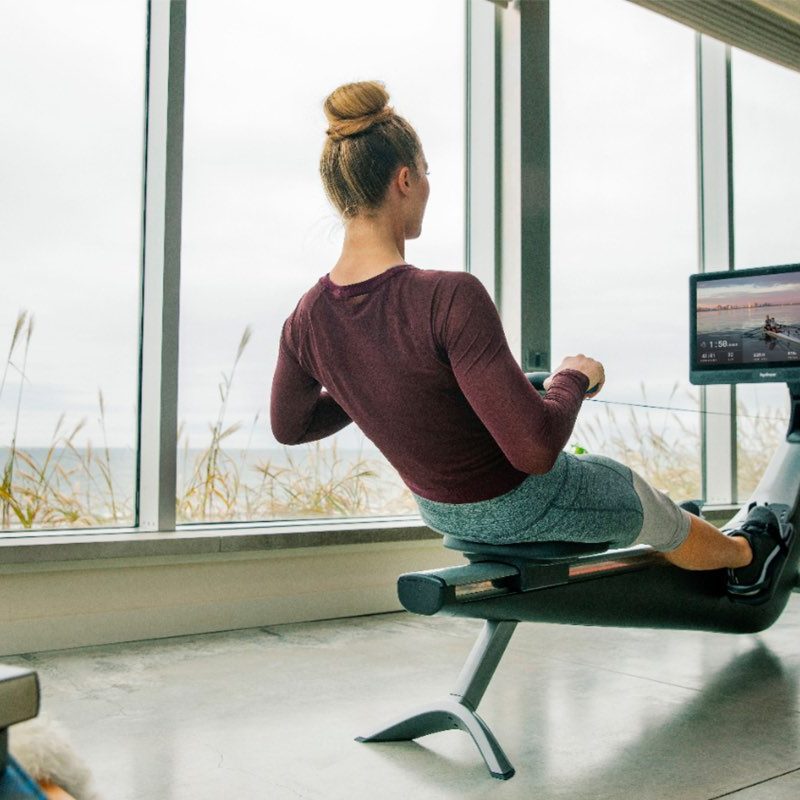 A woman does rowing exercises on her Hydrow Connected Rower.