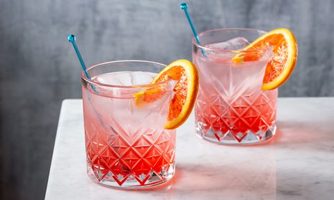 Two ice-cold glasses of gin with blood orange garnish with cocktail sticks on a table