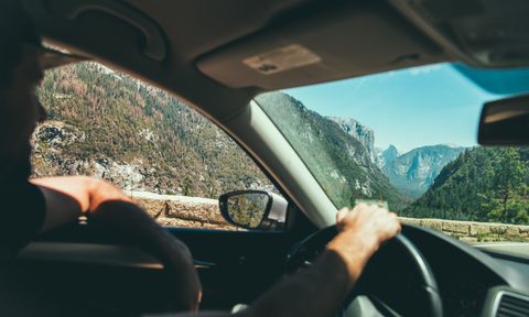A man drives a car through a hilly landscape while listening to the HearHere app.