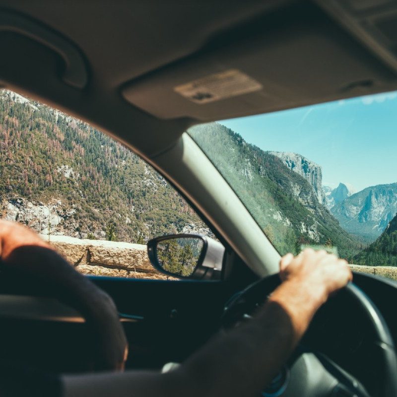 A man drives a car through a hilly landscape while listening to the HearHere app.