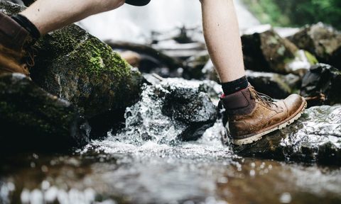Person in hiking boots crossing stream in the woods.