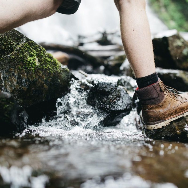 Person in hiking boots crossing stream in the woods