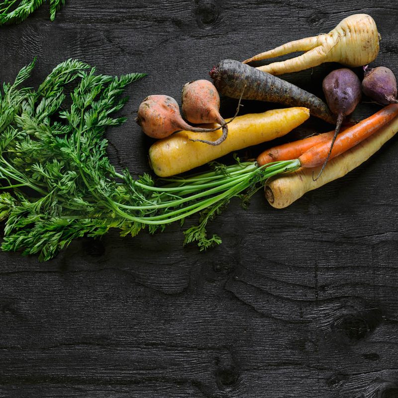 Assorted root vegetables on black table.