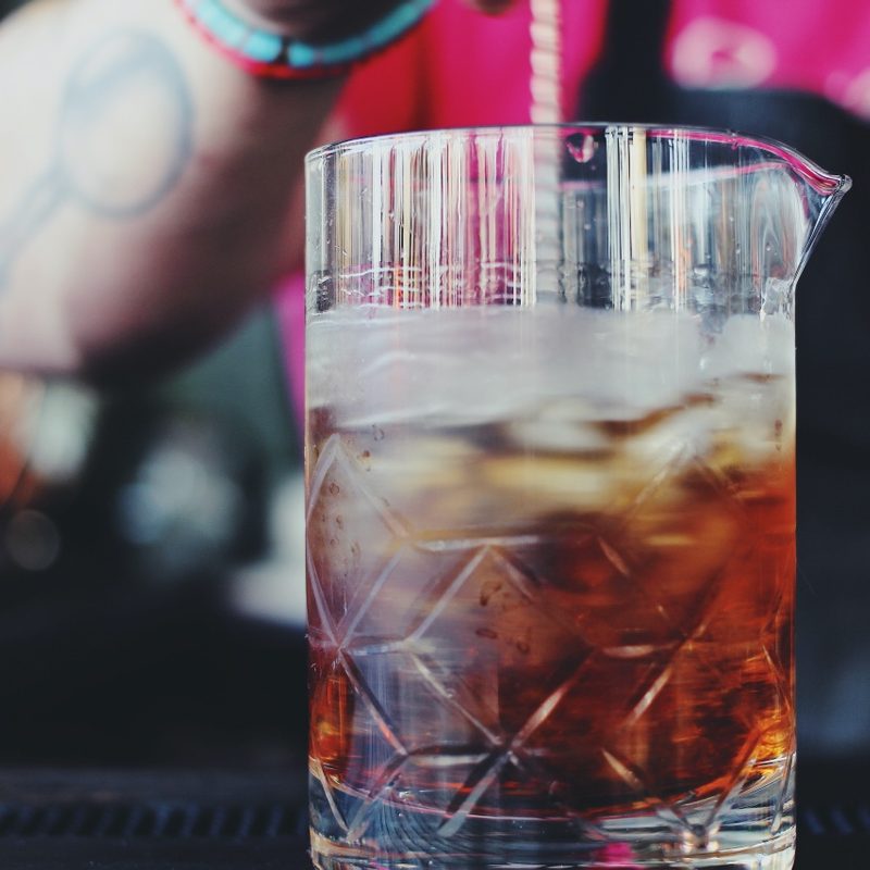 A bartender stirs a cocktail in a mixing glass.