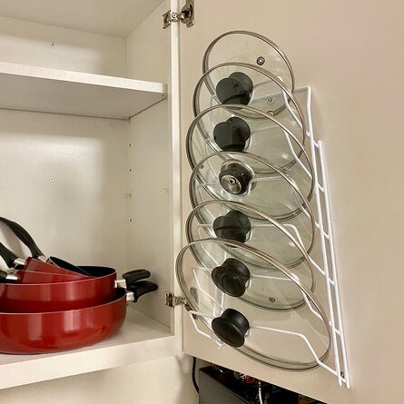 Pot and pan lids are stored on a rack inside of a cabinet. 