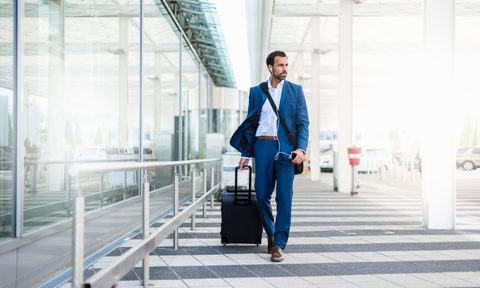 A man in a suit listening to music while hauling his luggage in the airport