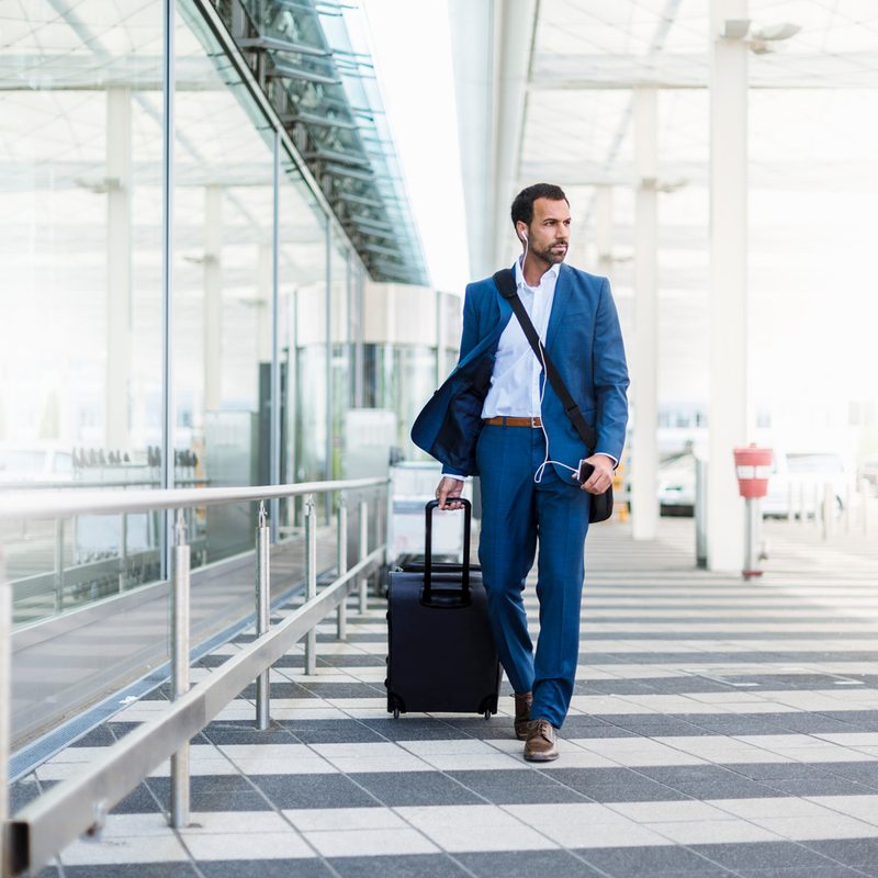 A man in a suit listening to music while hauling his luggage in the airport.