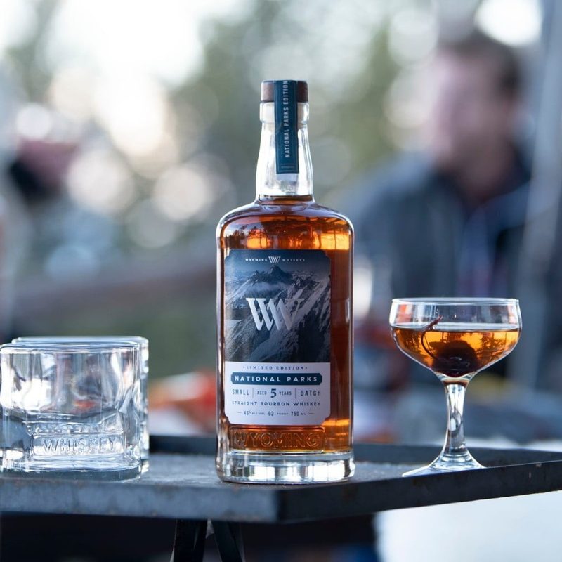 A bottle of Wyoming Whiskey National Parks Limited Edition whiskey on a table with cocktail glasses.