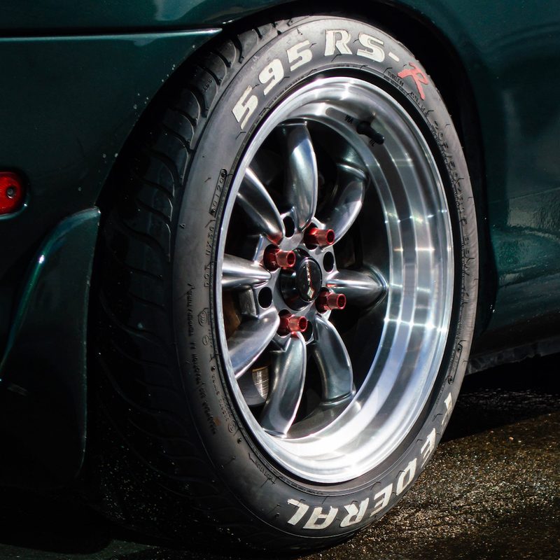 Close-up of rear tire on green muscle car with red lug nuts in a puddle of water on asphalt.