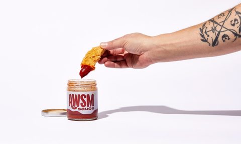 A man's arm dips a chicken tender into AWSM ketchup.