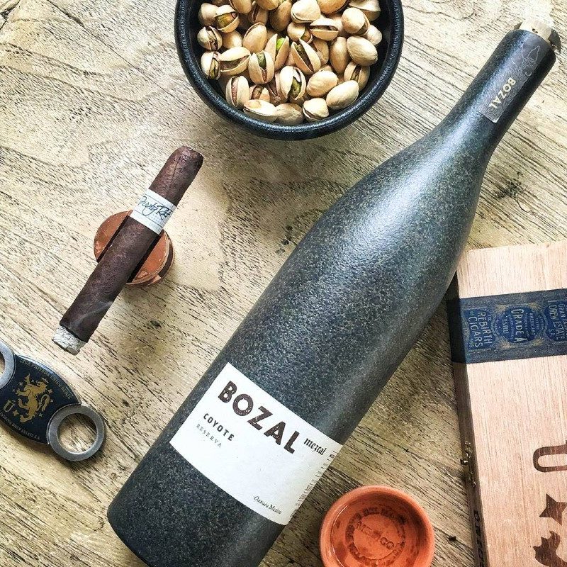 Bozal Chocolate Coyote Mezcal accompanied by nuts and a cigar.