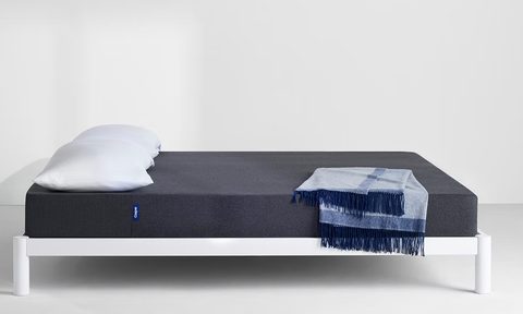 Casper mattress made up with sheets, blanket, and a blue throw blanket