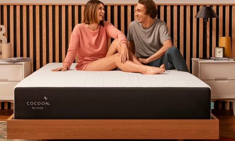 A couple sit on a sealy hybrid mattress in a bedroom.