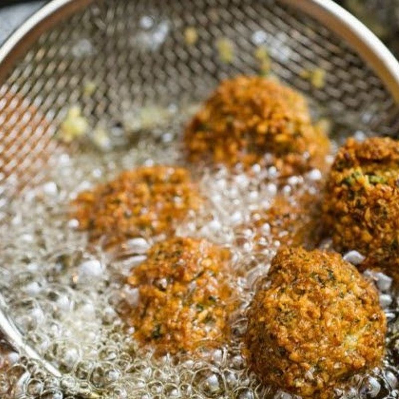 Hawajj-seasoned falafel in oil and a colander.
