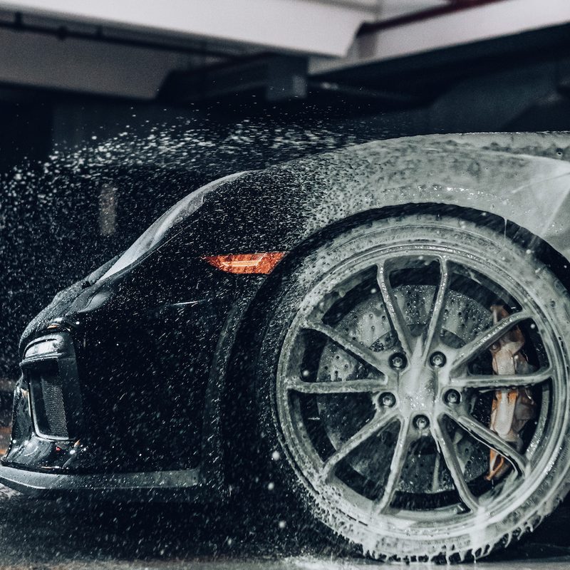 Close-up of front end tire of black Porsche 911 being washed with a spray foam gun