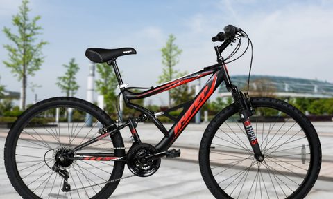 Hyper Bicycles 26-inch Shocker Mountain Bike parked on a street with blue sky, trees, and a small mountain in the background.