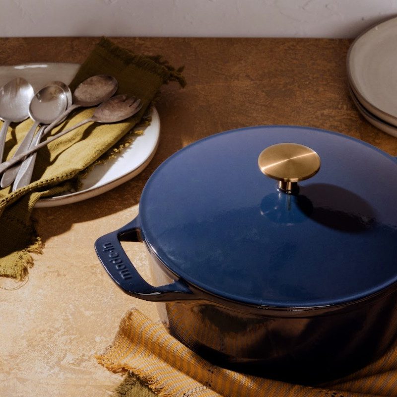 Blue dutch oven sitting on a counter with dishes and flatware