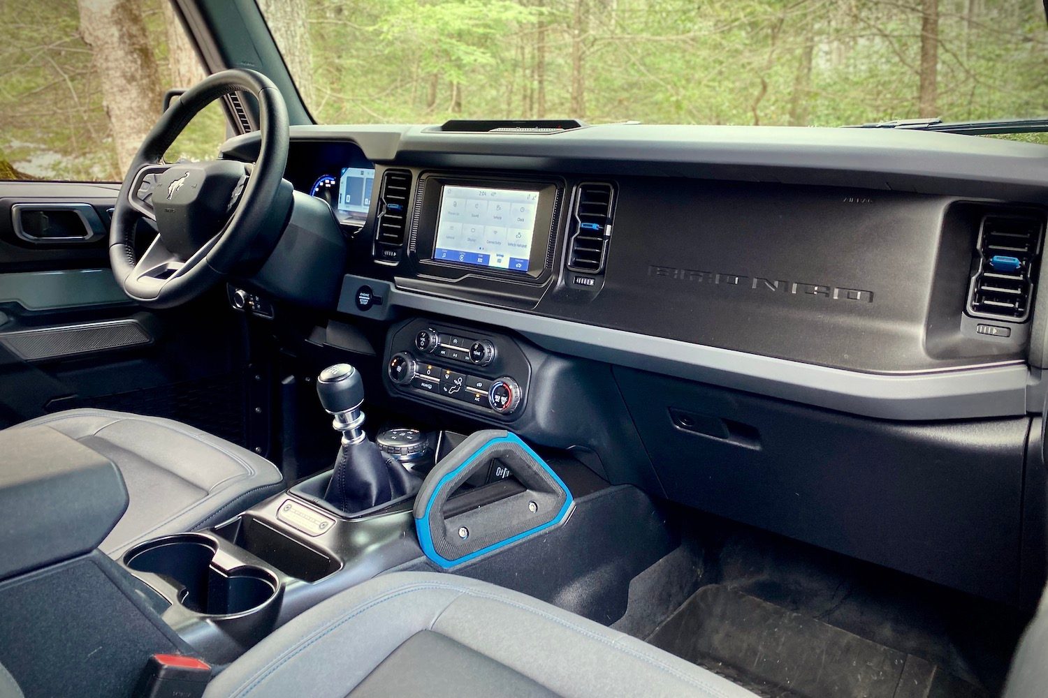 Dashboard and center console in 2021 Ford Bronco from passenger side with trees in the back.