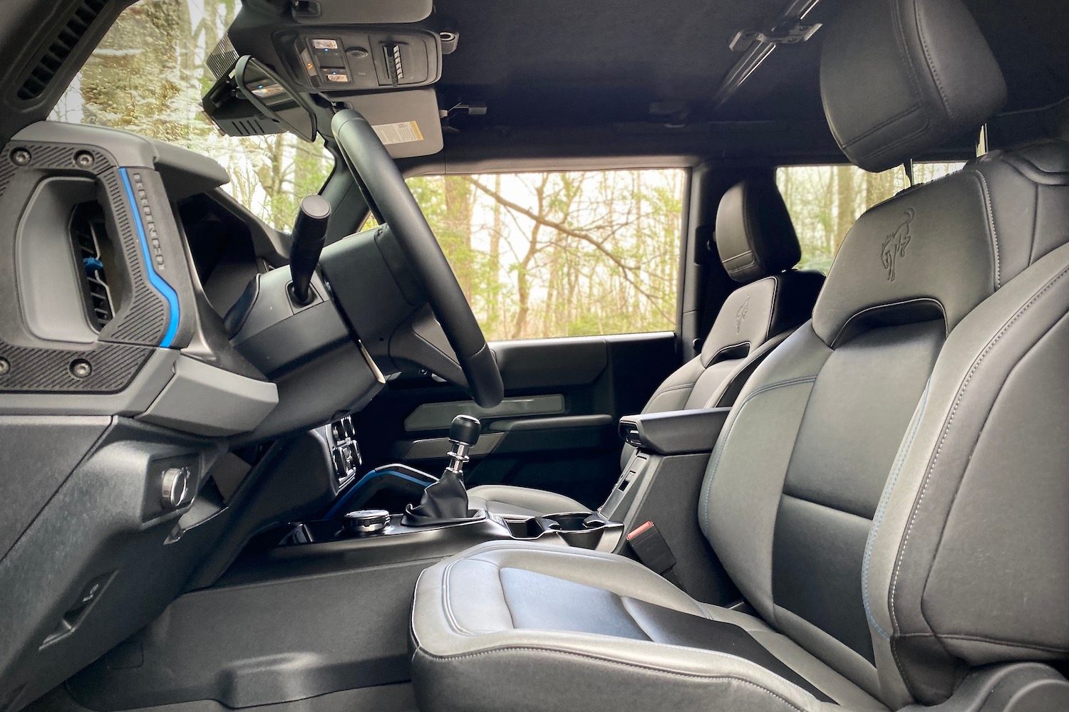 Side view of front seats in 2021 Ford Bronco from driver's side with trees in the back.