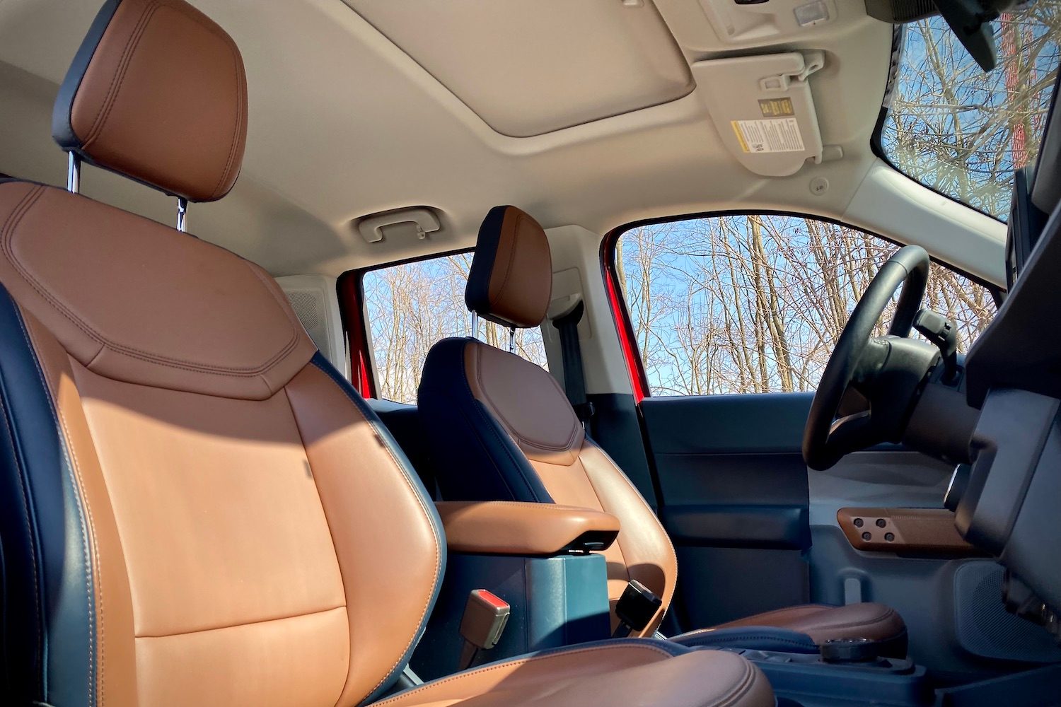 Front seats in the 2022 Ford Maverick from passenger side with blue skies and trees in the back.