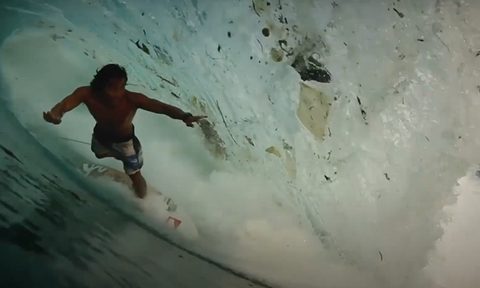 A surfer rides a wave littered with garbage
