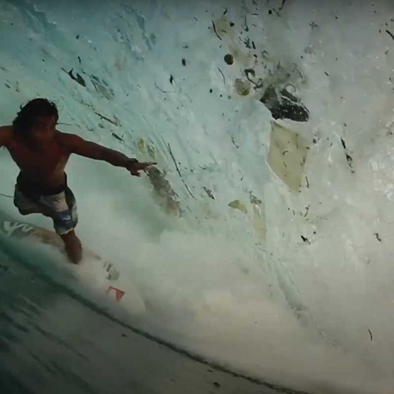 A surfer rides a wave littered with garbage