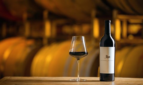 A bottle of My Favorite Neighbor wine next to a glass with casks in the background.
