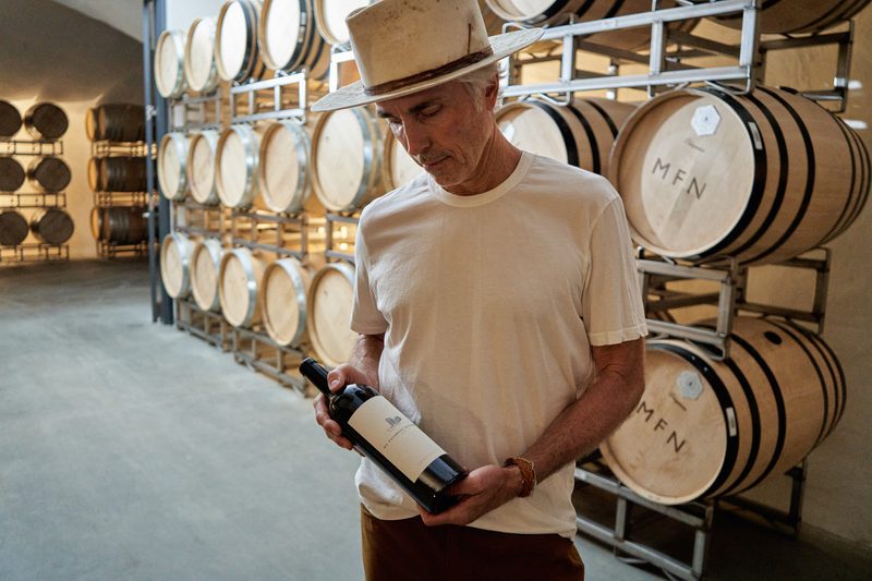 My Favorite Neighbor wine founder Eric Jensen holds a bottle of wine with casks in the background.