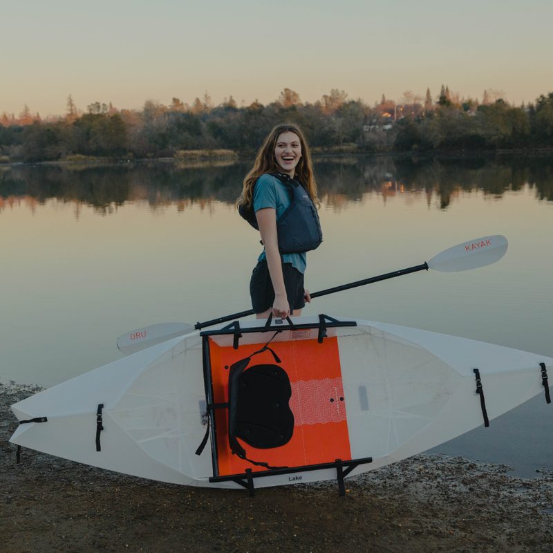 Woman carrying an Oru folding kayak with one hand