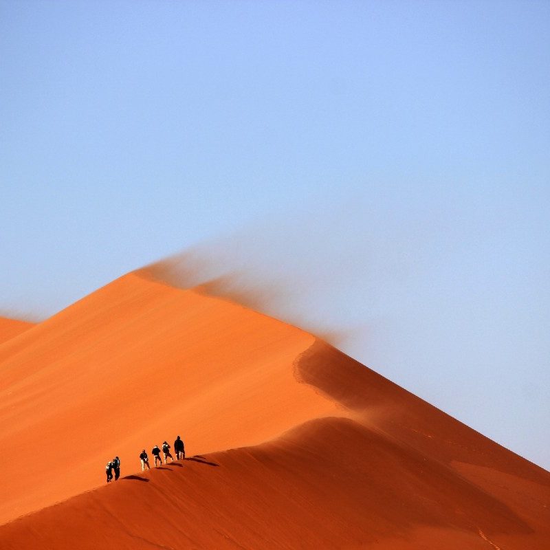 Small group of people hiking the red dunes in Dubai.