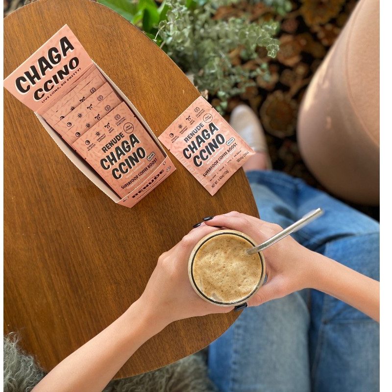 Renude Chagaccino packages next to a hand holding a cold-brewed glass of the mushroom mix