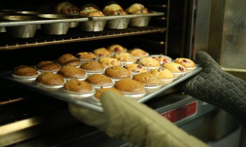 Removing muffins in a metal baking dish from the oven