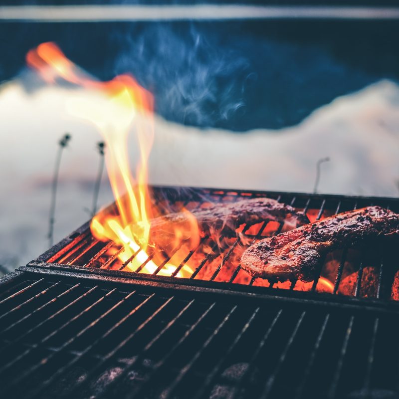 Two steaks cooking on a grill on an open fire.