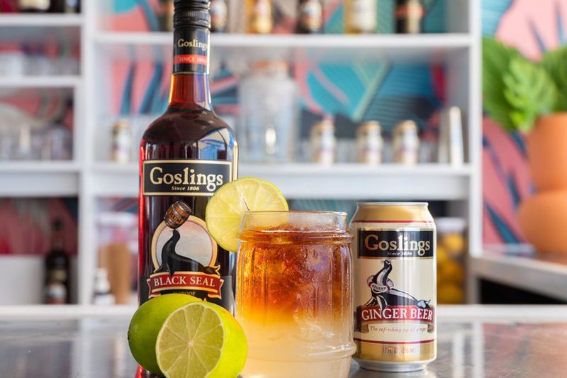 A Goslings Dark 'n' Stormy surrounded by lime, Black Rum, and Ginger Beer ingredients