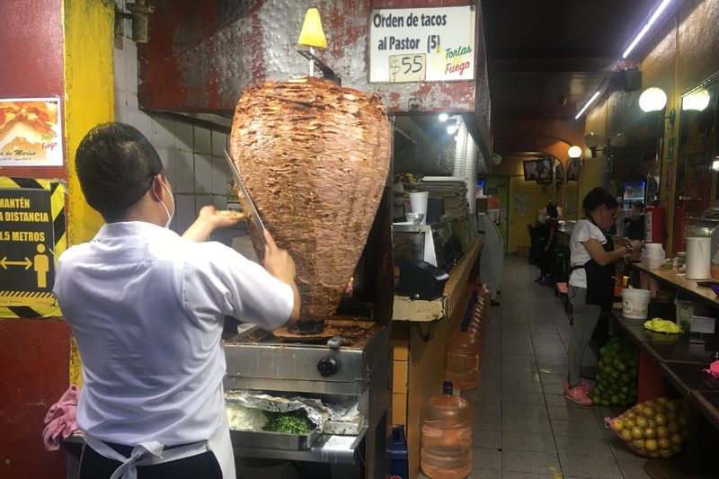 A cook slices al pastor meat off of a trompo in Mexico City