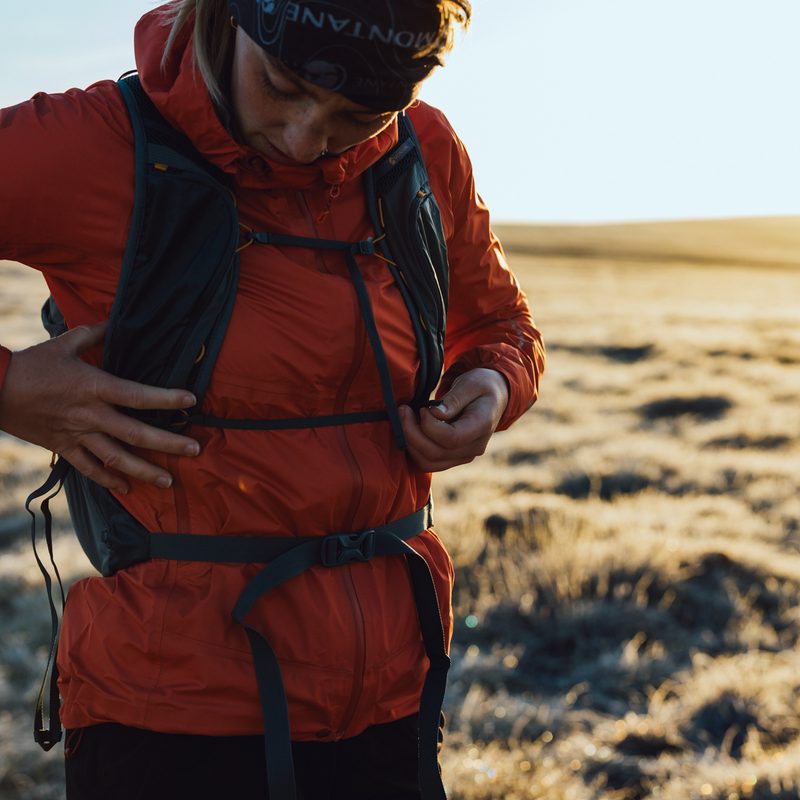 A close-up shot of a person wearing a red jacket and adjusting the chest band on their backpack