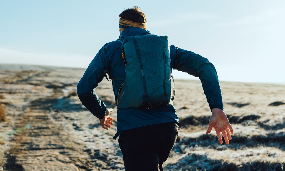 A close-up shot of a man running away from the camera. He is wearing blue jacket and carrying a blue backpack