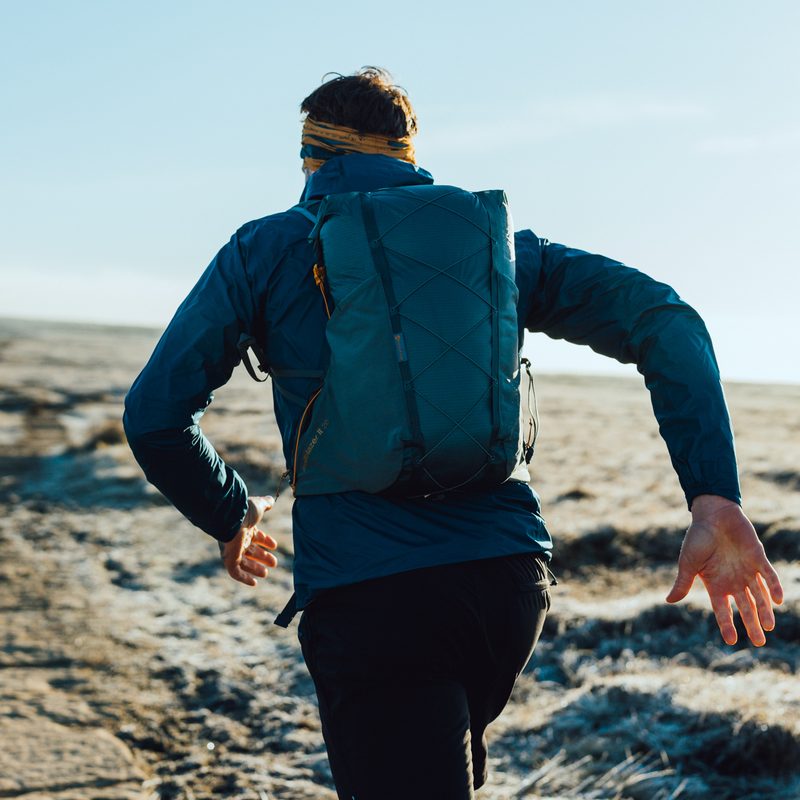 A close-up shot of a man running away from the camera. He is wearing blue jacket and carrying a blue backpack