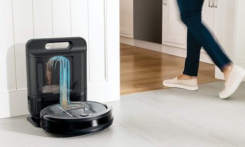 Person walking by self-emptying Shark IQ robot vacuum at docking station