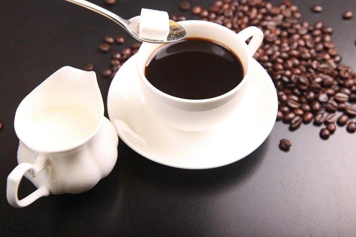 Black coffee with a sugar cube being added.