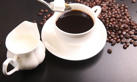 Black coffee with a sugar cube being added.