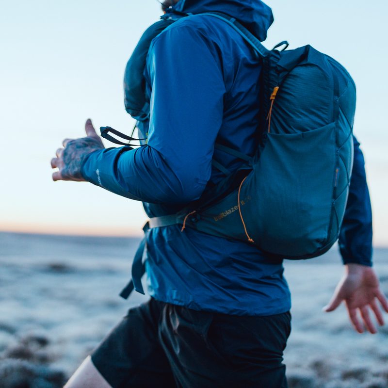 A close-up shot of the left hand side of a person running, wearing shorts and a blue jacket and carrying a small backpack