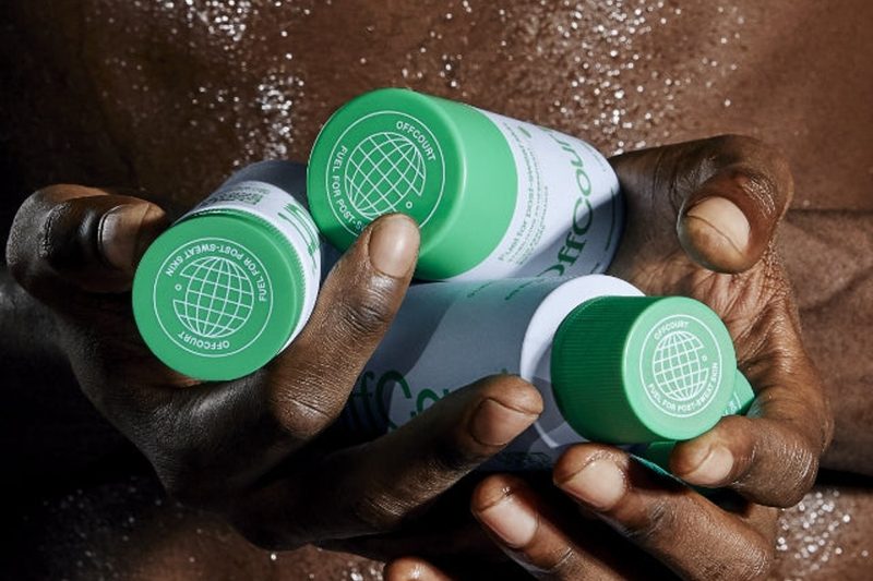 A man holds three cans of OffCourt Performance Body Spray.