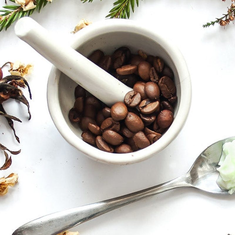 A small bowl of coffee beans and a spoon full of cocoa butter