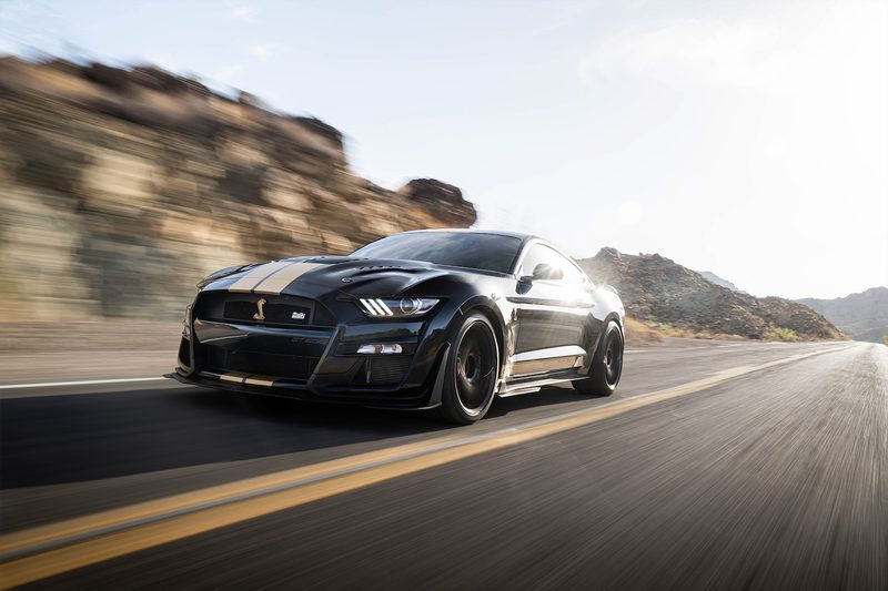2022 Shelby GT500-H driving on a two-lane road with mountains in the background with sun shining on the back end.
