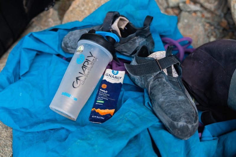 A climbing shoe next to an empty Gnarly water bottle and electrolyte bar.