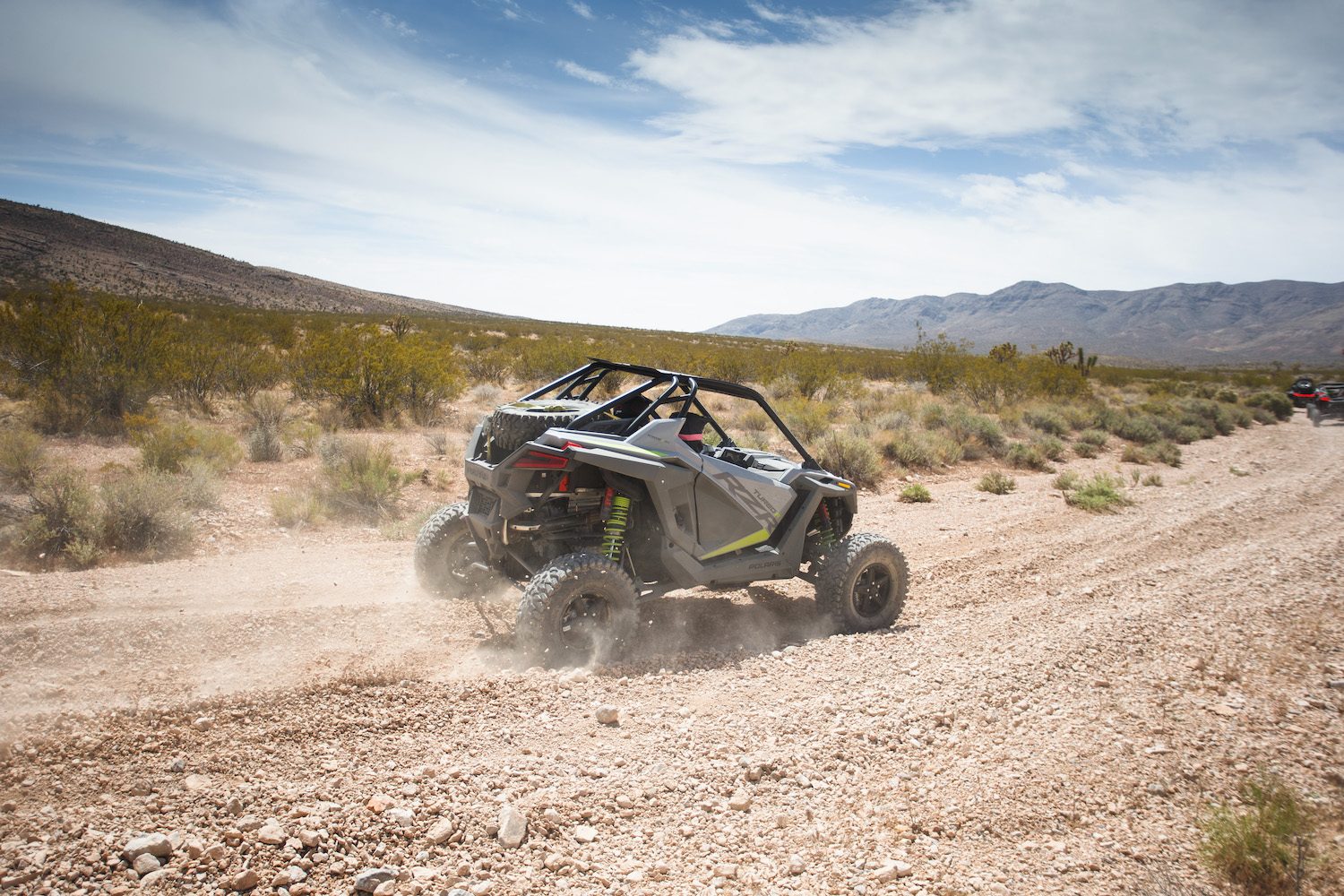 Rear end angle of Polaris RZR Turbo R on a dirt trail in the desert with mountains in the background.