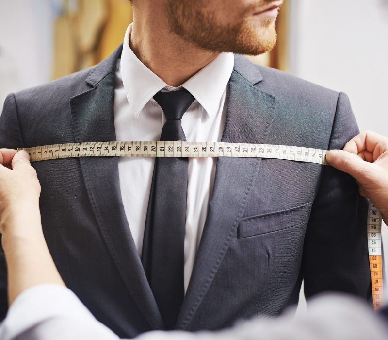 Tailor stretching measuring tape across suited chest