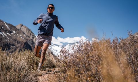 A man in sunglasses runs downhill past a close up image of heather.