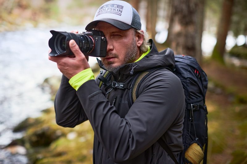A hiker in a Jack Wolfskin jacket pointing a camera.